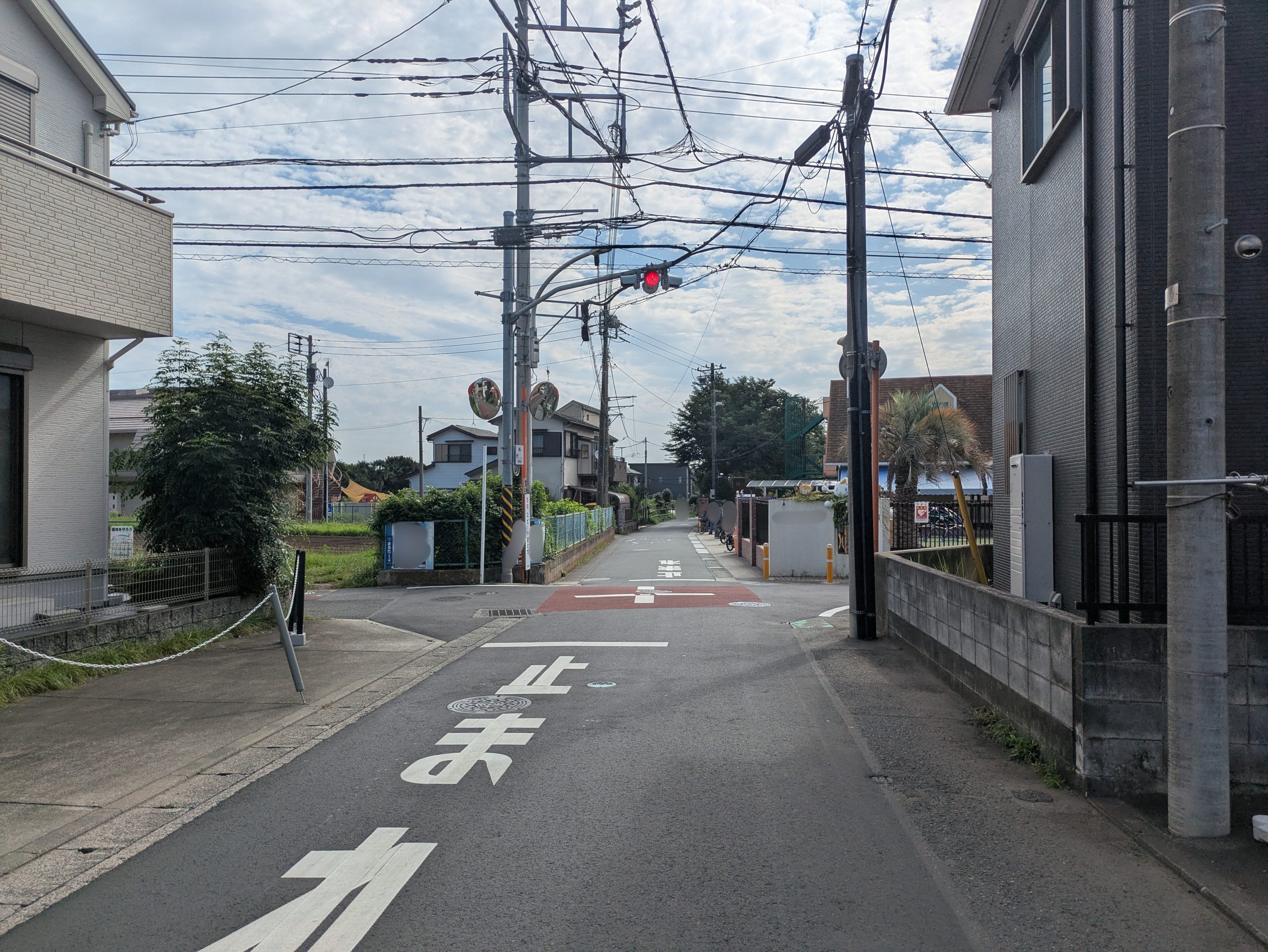 住宅地の交差点。赤いランプが点滅する一灯点滅式信号、路面の「止まれ」の表示、赤い舗装、「危険 スピードおとせ」の看板
